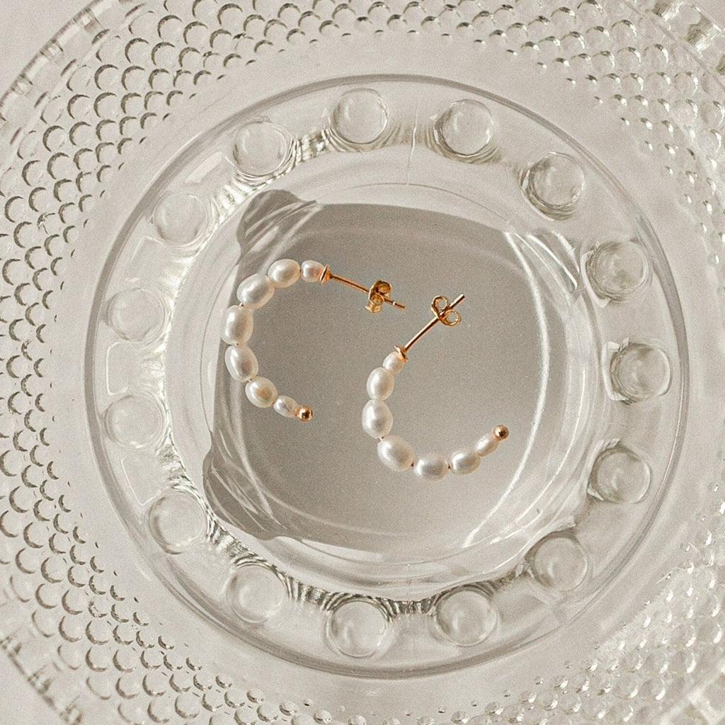 Pearl Hoops are displayed on a clear textured glass plate, highlighting these earrings as an elegant everyday accessory.
