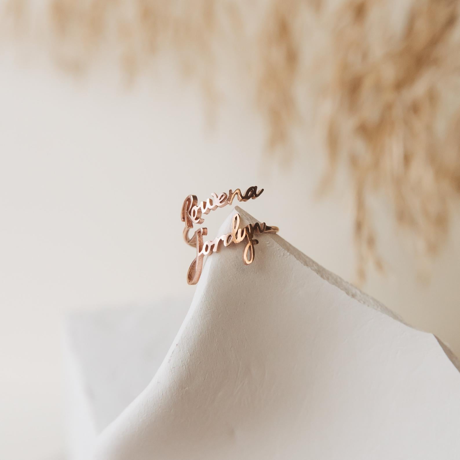 The Grace Duo Name Ring, personalized with "Rowena" and "Jordyn" in elegant cursive, is shown on a white surface.