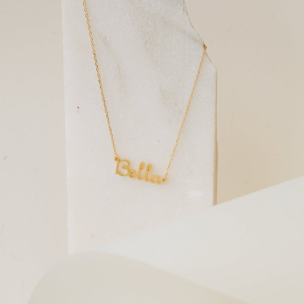 Dainty Name Necklace shown with "Bella" lettering on a light marble background—an ideal minimalist accessory for adding personalized style.