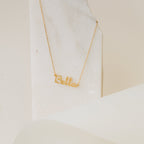 Dainty Name Necklace shown with "Bella" lettering on a light marble background—an ideal minimalist accessory for adding personalized style.