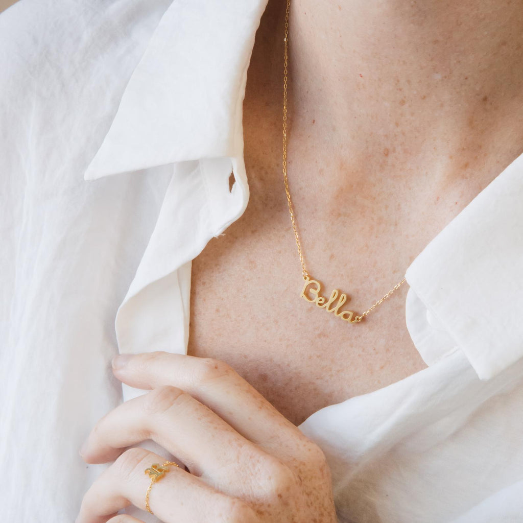 A person in a white shirt wears the Dainty Name Necklace and a gold ring, highlighting minimalist jewelry style with personalized elegance.