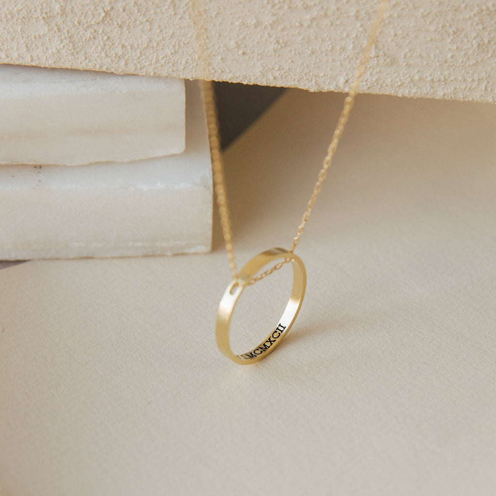 The Inner Circle Necklace in gold showcases a circular pendant engraved with "NICHOLE," set against a neutral background.