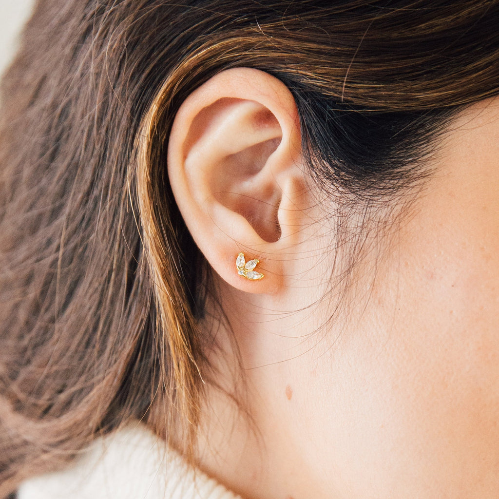 Close-up of Arya Petal Studs—gold and diamond leaf-shaped earrings—worn on a woman's ear with brown hair.