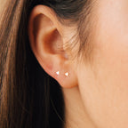 Close-up of a persons ear with two Tiny Heart Studs in 18K Gold; brown hair partially visible—perfect for everyday wear or as a thoughtful gift.