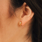 A close-up of a woman's ear wearing Enya Huggies—small gold diamond huggie earrings accented with an iridescent diamond set in a star-shaped prong.