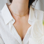 A woman wears a white shirt and the Paperclip Toggle Necklace in Rose Gold, with a white flower in the foreground, creating a chic boho look.