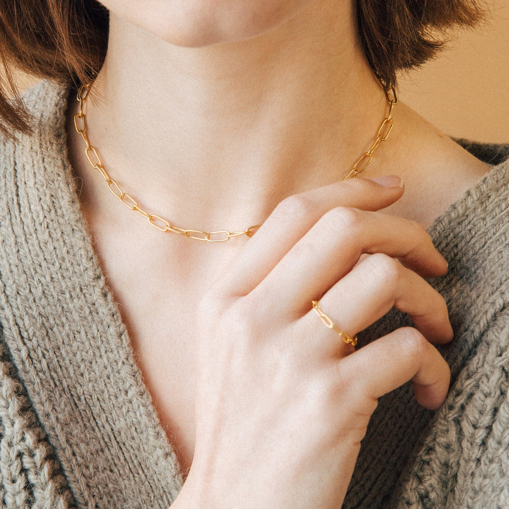 Woman wearing the Paperclip Toggle Necklace, paired with a gold ring and a beige knit sweater, for a subtle boho-chic vibe.