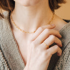 Woman wearing the Paperclip Toggle Necklace, paired with a gold ring and a beige knit sweater, for a subtle boho-chic vibe.
