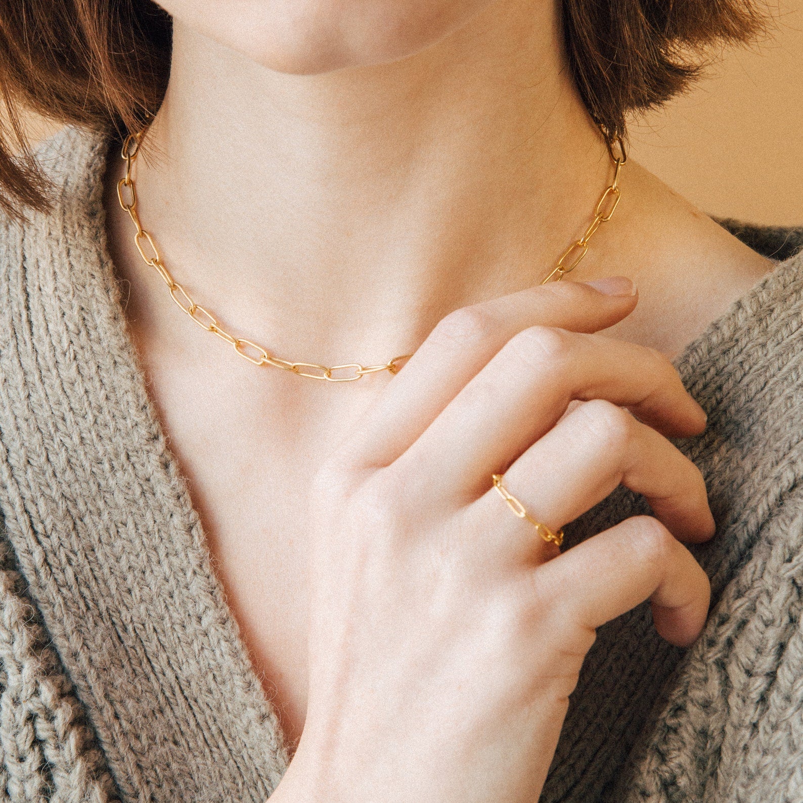 Woman wearing the Paperclip Toggle Necklace, paired with a gold ring and a beige knit sweater, for a subtle boho-chic vibe.