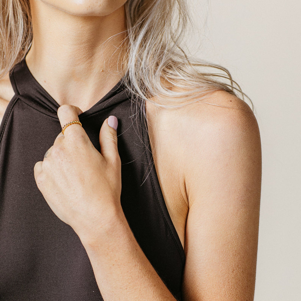 A woman in a black sleeveless top holds the neckline with her left hand, highlighting the Tia Twisted Ring—a modern piece ideal for creating a bold finger stack.
