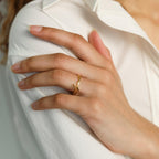A manicured hand wearing the Venice Name Ring rests on a white shirt sleeve; natural nails enhance the refined elegance of this custom jewelry piece.