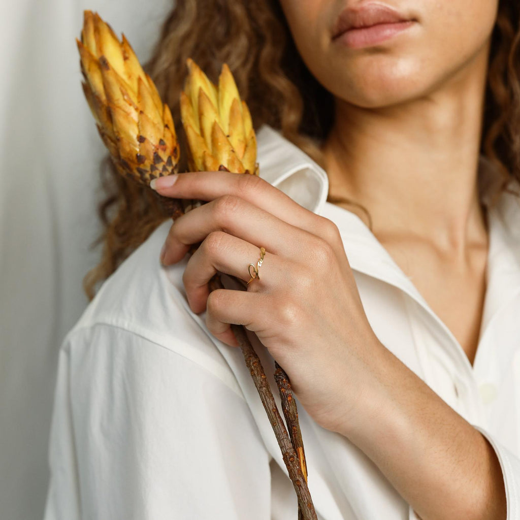 Woman in white shirt holding two yellow protea flowers, wearing a delicate gold ring and a personalized Venice Name Ring.