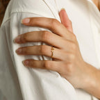 A hand with natural nails wears the Modern Duo Initial Ring, a delicate personalized piece, resting on a white shirt sleeve.