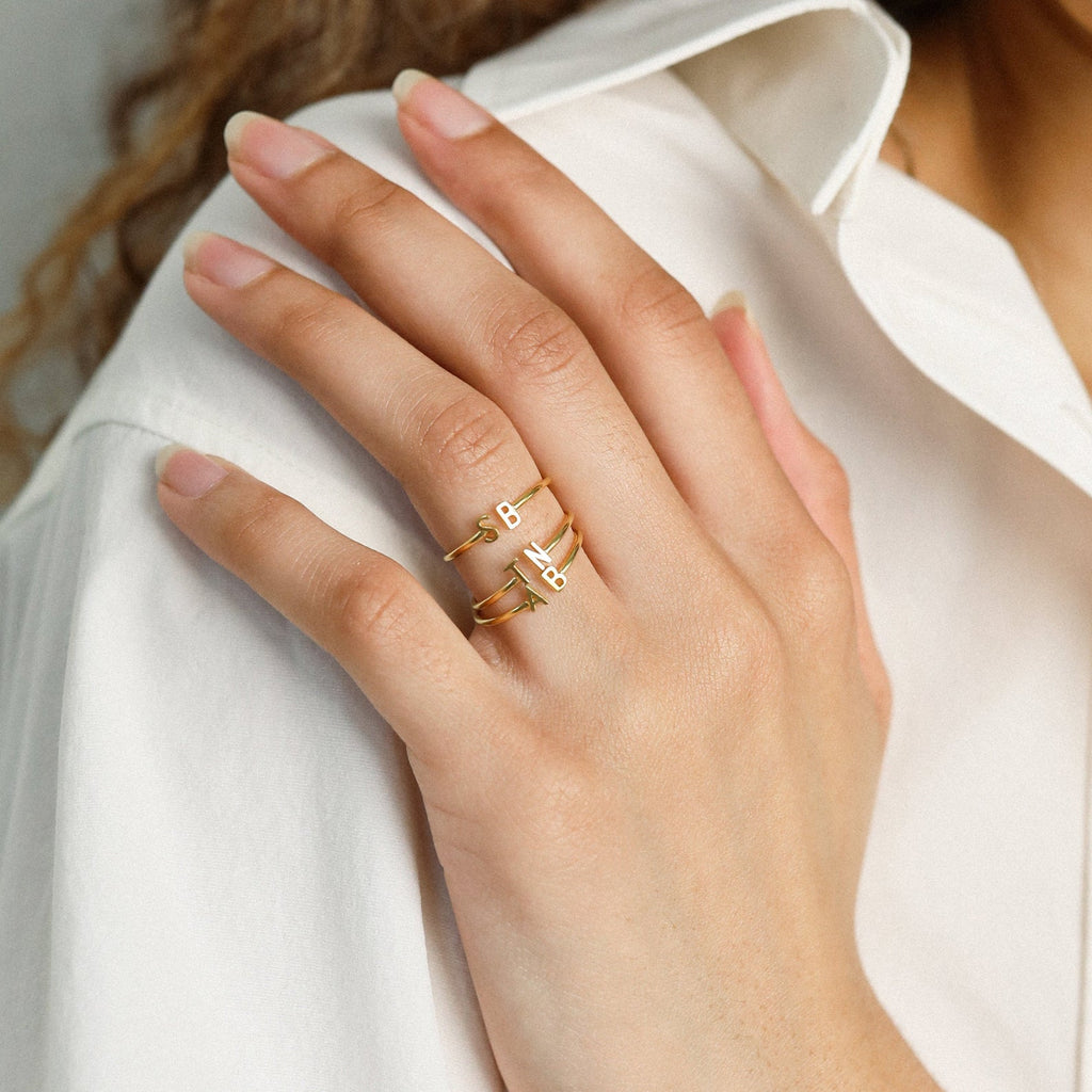 A hand adorned with the Modern Duo Initial Ring, showcasing gold initials A and B, rests elegantly on a white shirt.