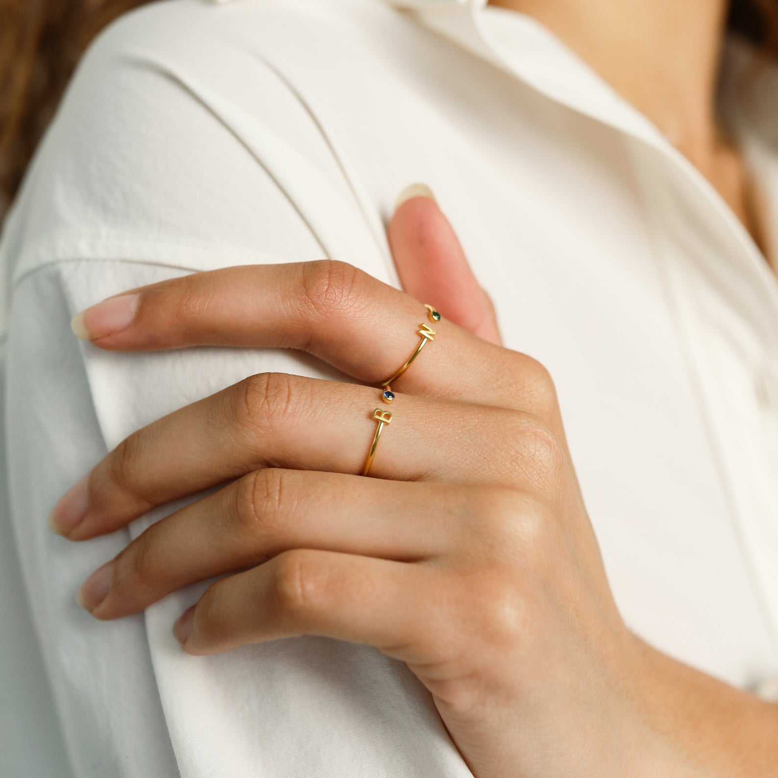 Close-up of a hand wearing gold rings, including the Modern Initial Birthstone Ring, resting on a collared white shirt.