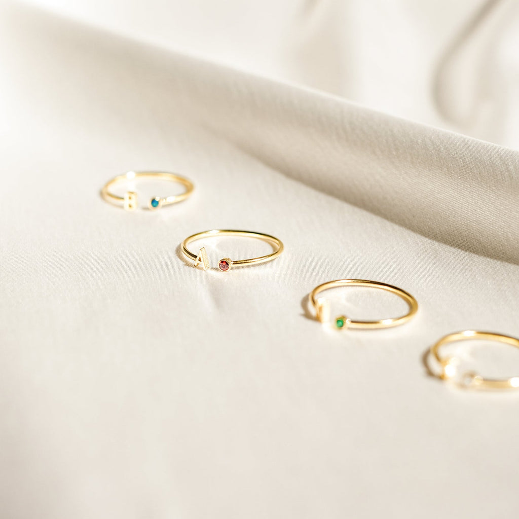 Four dainty Modern Initial Birthstone Rings, each with a unique gemstone, displayed on soft cream fabric—an ideal customizable ring set or meaningful Christmas gift.