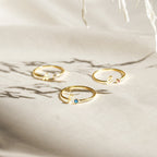 Three gold Venice Initial Birthstone Rings rest on light fabric, each with a delicate gemstone and cursive lowercase letter charm—a personalized ring, perfect as an initial birthstone accessory for everyday elegance.