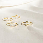 Four delicate Zodiac Birthstone Rings with colorful gemstones are displayed on soft ivory fabric, creating an elegant jewelry statement.
