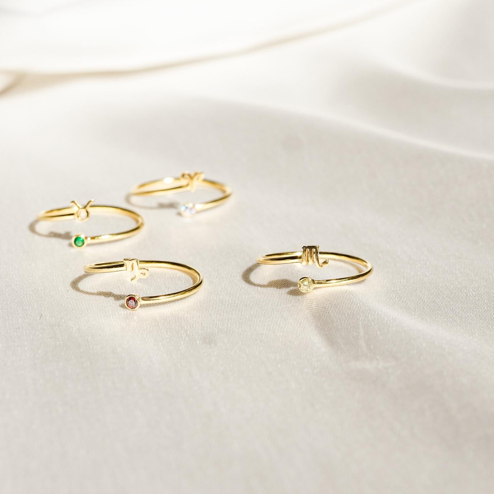 Four delicate Zodiac Birthstone Rings with colorful gemstones are displayed on soft ivory fabric, creating an elegant jewelry statement.