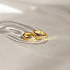 Two Ann Half Round Rings engraved with the names Stella and Loraine rest on soft, light fabric. Each personalized band highlights timeless elegance and meaning.