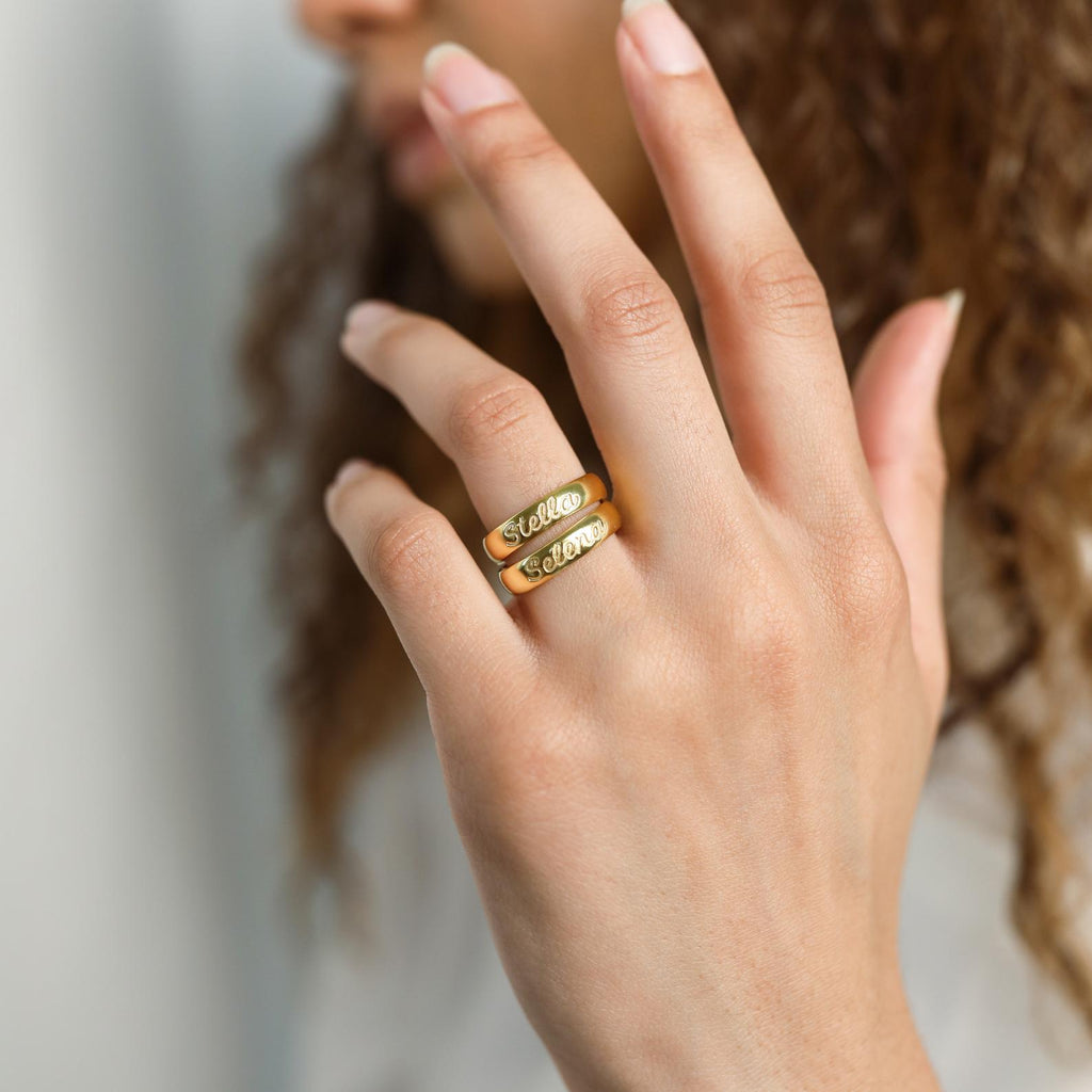 Two gold Ann Half Round Rings, personalized with engraved names, are worn on the index and middle fingers.