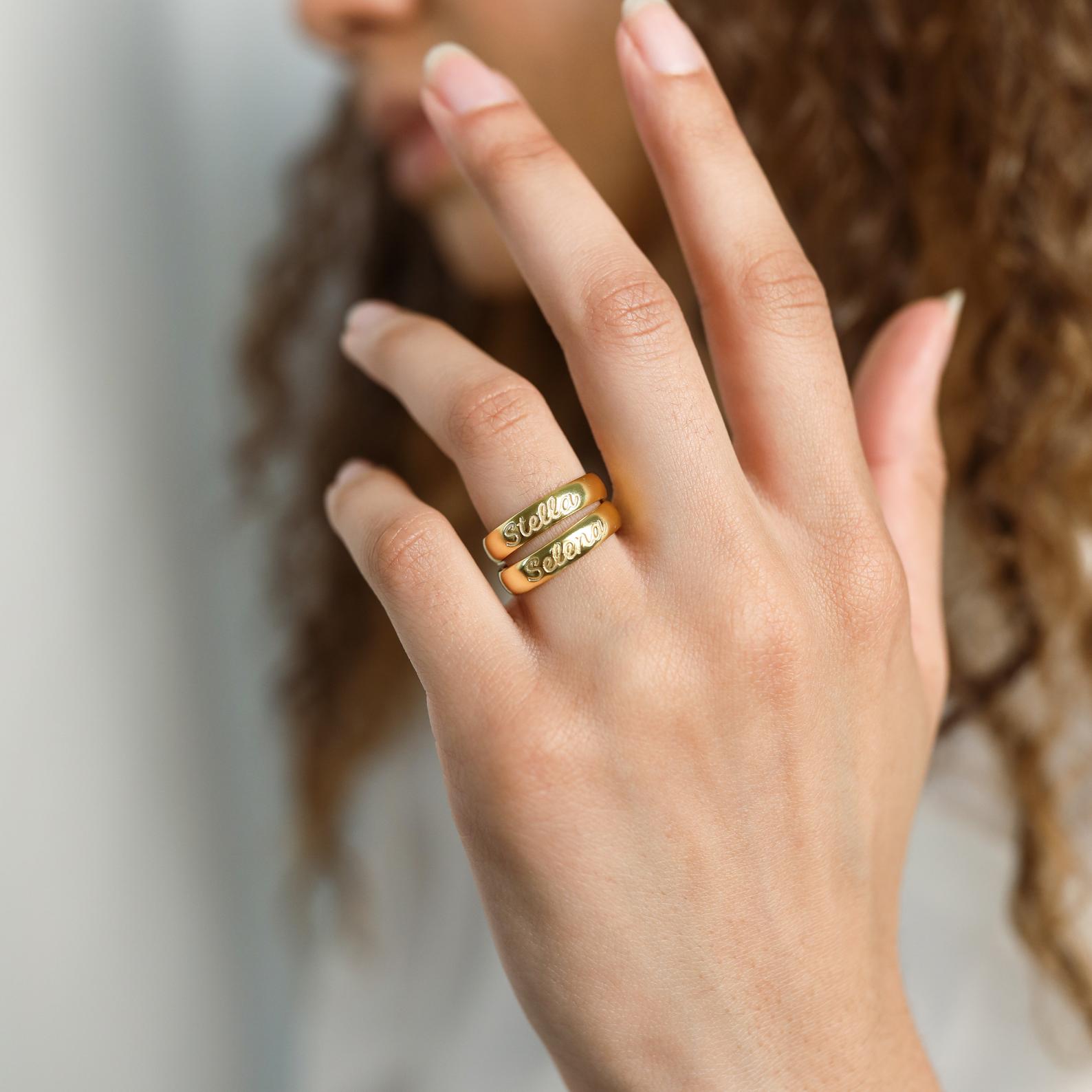 Two gold Ann Half Round Rings, personalized with engraved names, are worn on the index and middle fingers.