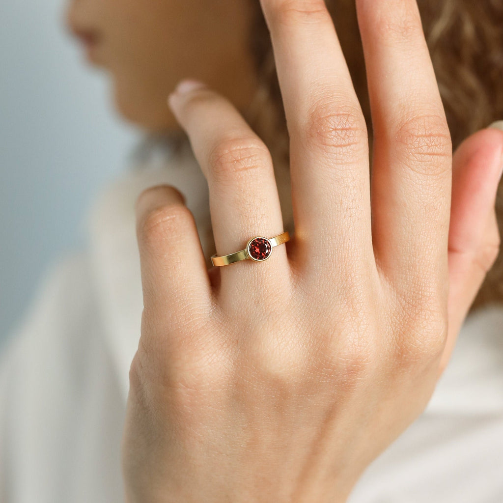 A hand wears the Birthstone Signet Ring, a gold vintage piece with a round red gemstone, fingers slightly curved.