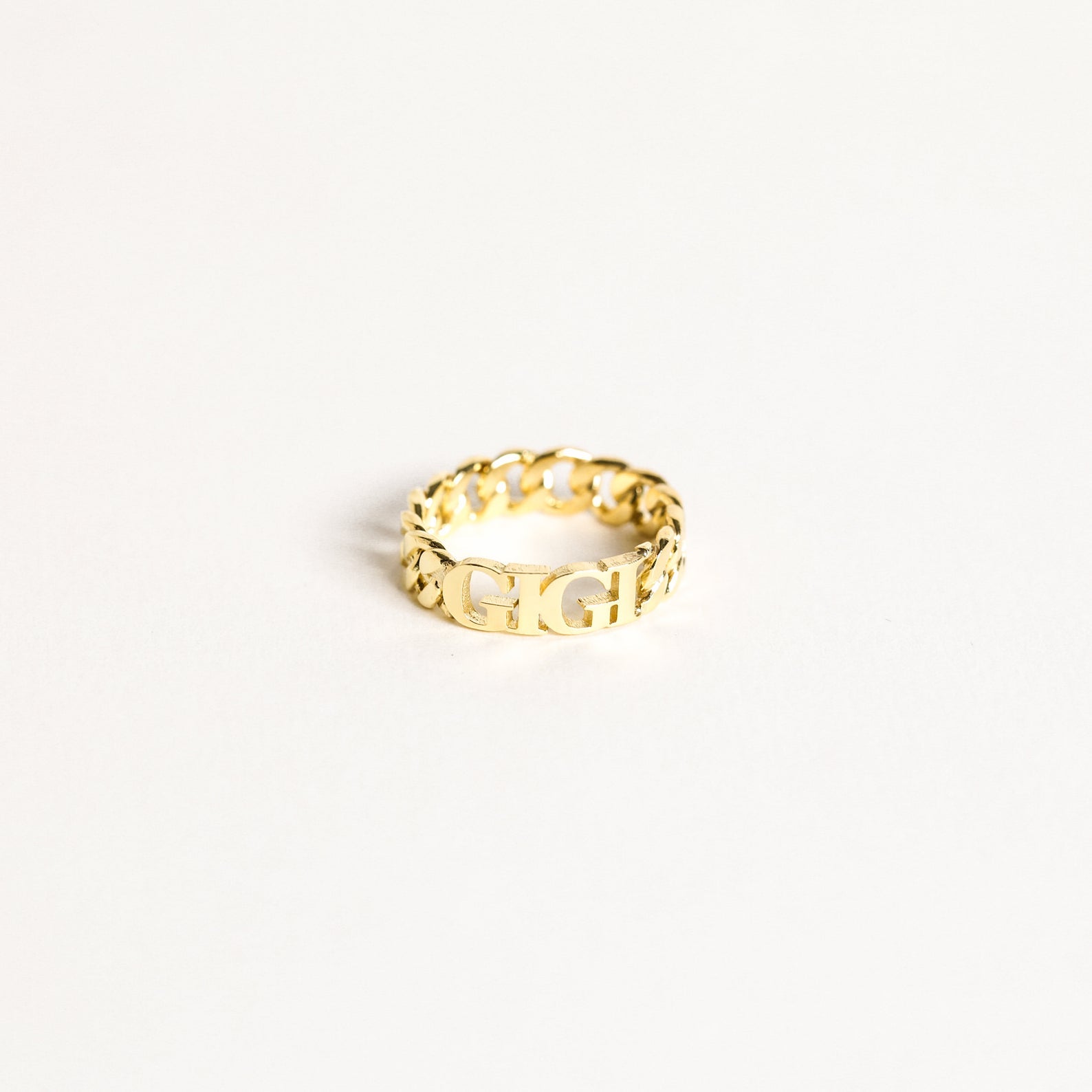 The Newsletter Curb Name Ring in Rose Gold features a gold chain design with personalized letters at the center, showcasing the classic curb name ring style against a plain white background.