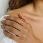 A person’s hand wearing the Newsletter Curb Name Ring gently rests on their bare shoulder, with a white garment visible.