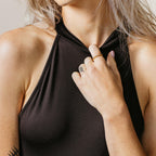 Woman in a sleeveless black top holds her collar, wearing the contemporary Tia Twisted Ring and showcasing a subtle finger stack, with a small finger tattoo adding to her chic look.