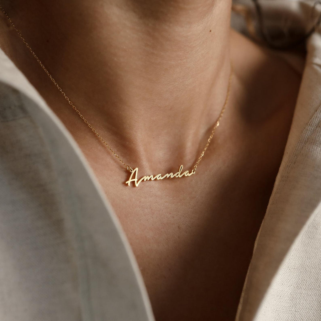 The Venice Name Necklace showcases the name "Amanda" in elegant script, creating a delicate accessory that's perfect to wear with a light-colored shirt.