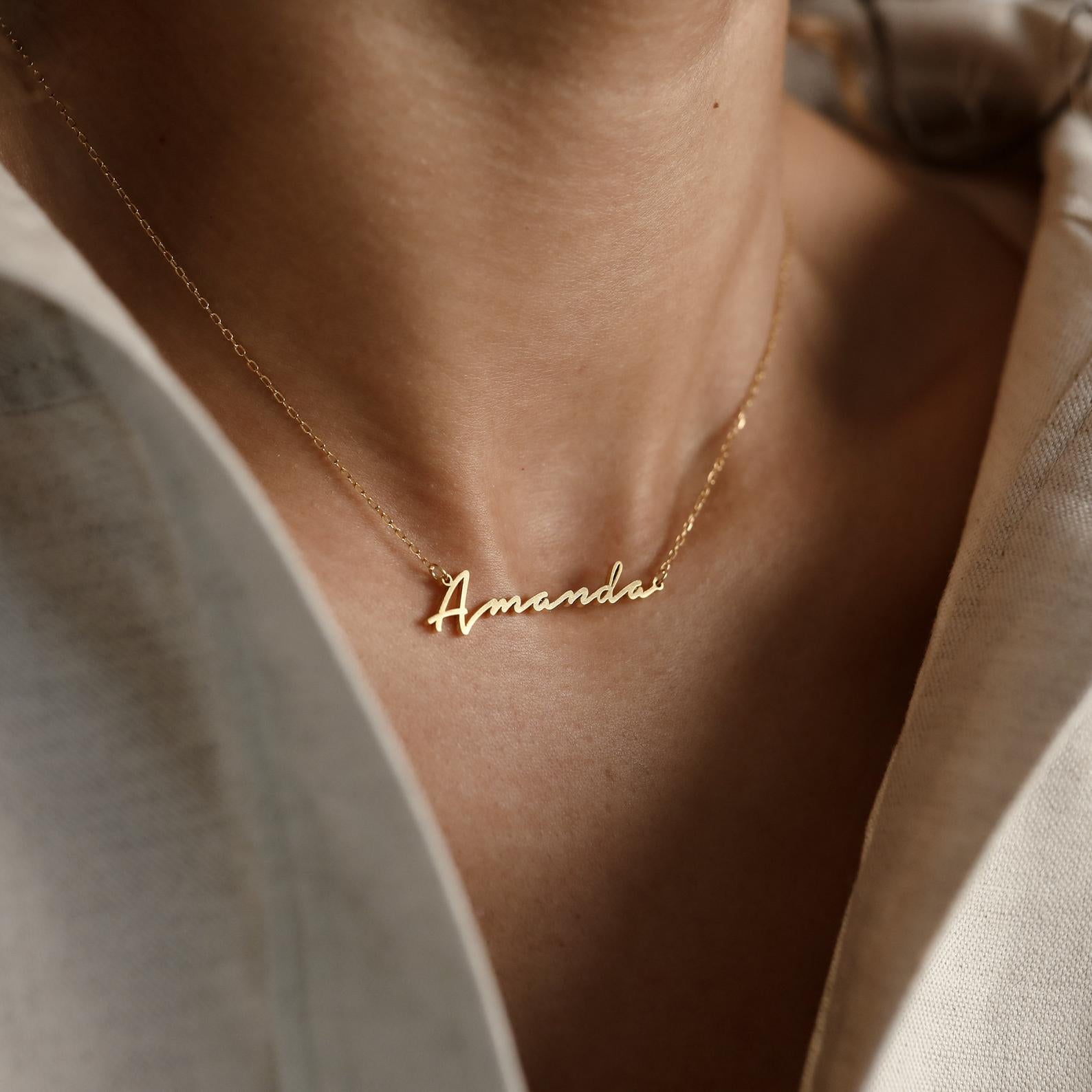 The Venice Name Necklace showcases the name "Amanda" in elegant script, creating a delicate accessory that's perfect to wear with a light-colored shirt.