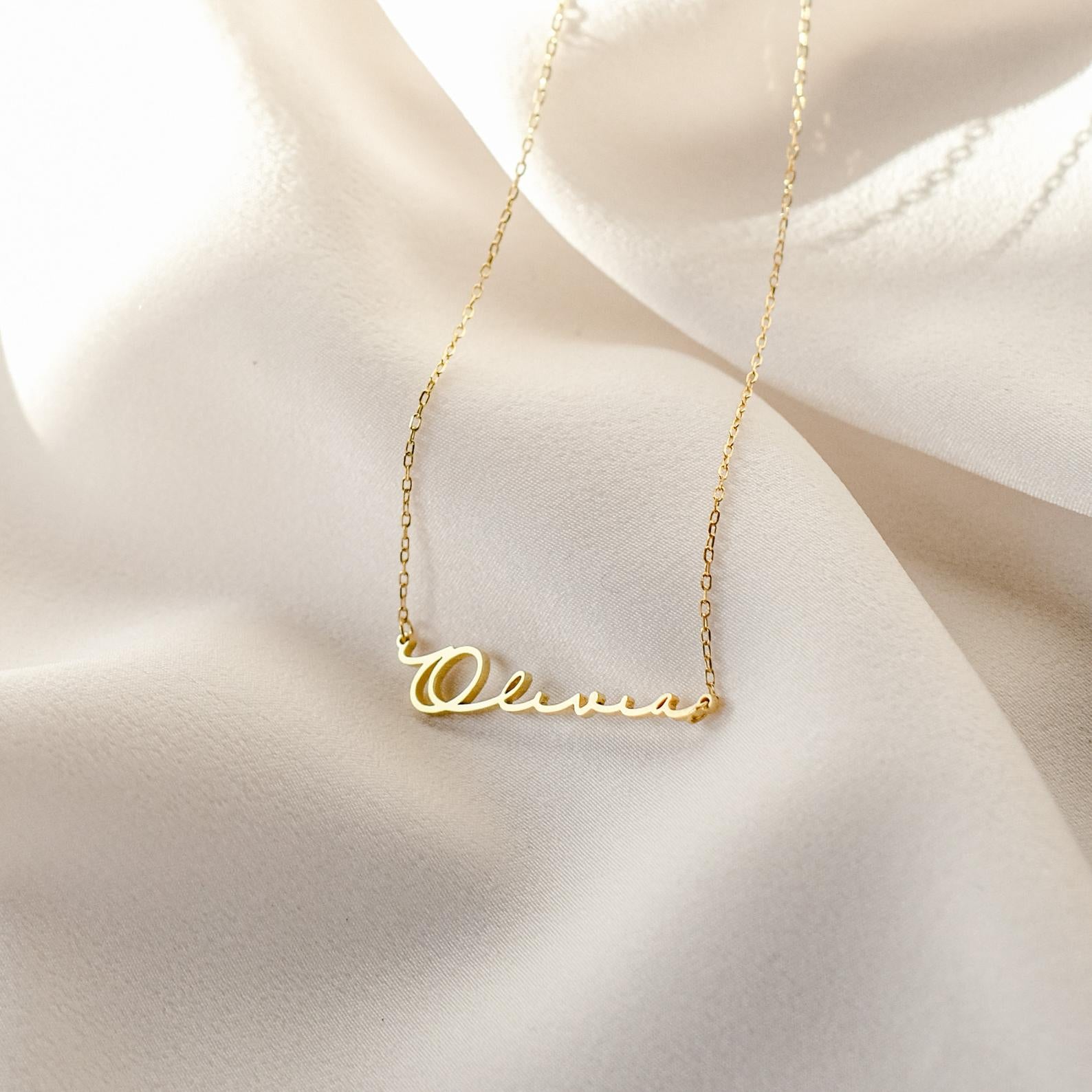 Minimal Name Necklace featuring "Olivia" in elegant cursive, shown on cream fabric—a beautiful personalized gift for any occasion. Available in gold or sterling silver.