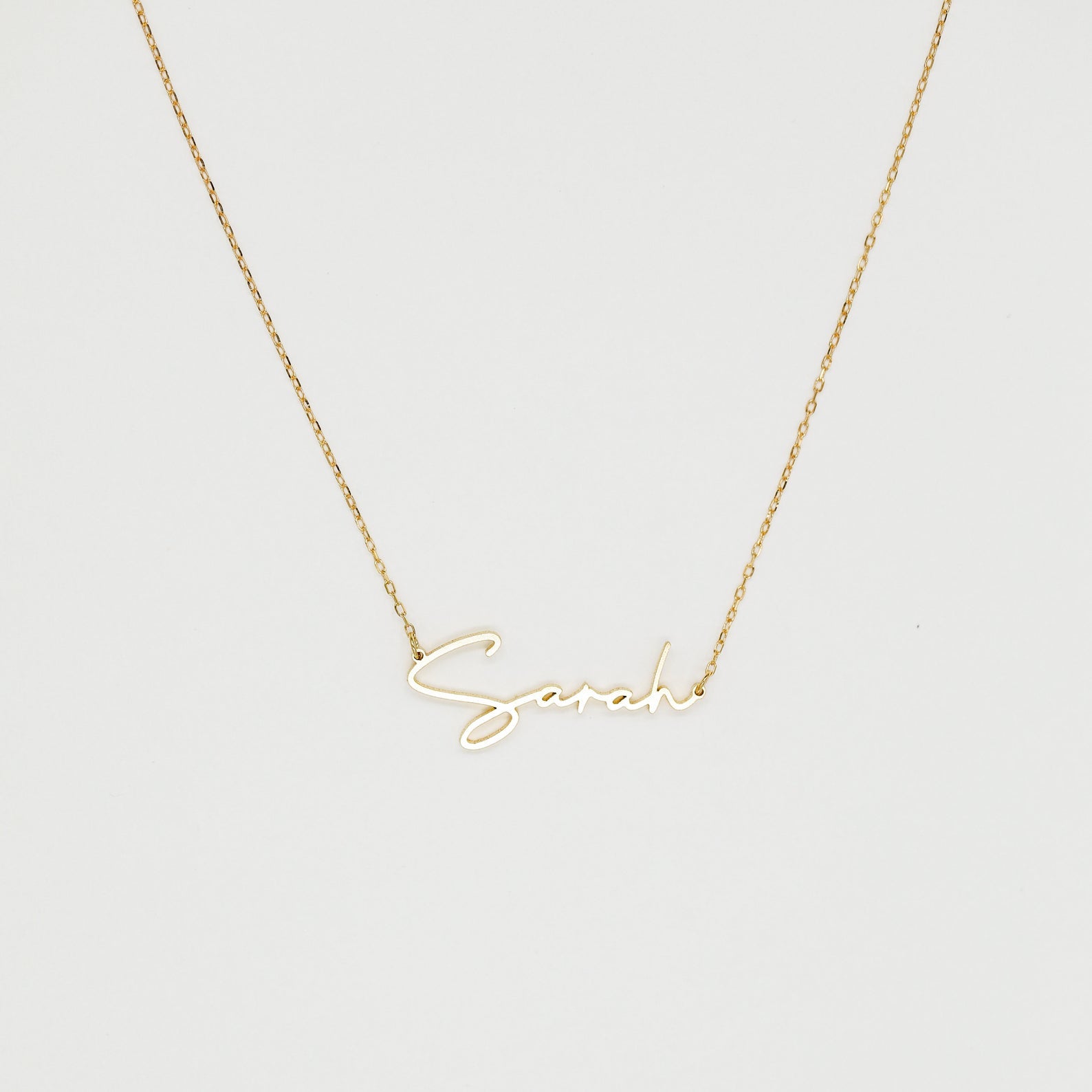 The Summer Name Necklace features a gold chain with a personalized pendant that spells "Sarah" in an elegant script font—perfect for any occasion.