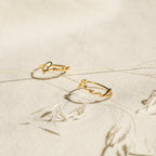 Two delicate Venice Name Rings with elegant cursive script rest on a textured cream surface, accented by dried plant stems.