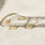Four delicate Venice Name Rings with cursive words rest on a light surface, casting soft shadows—a beautiful touch of custom jewelry.