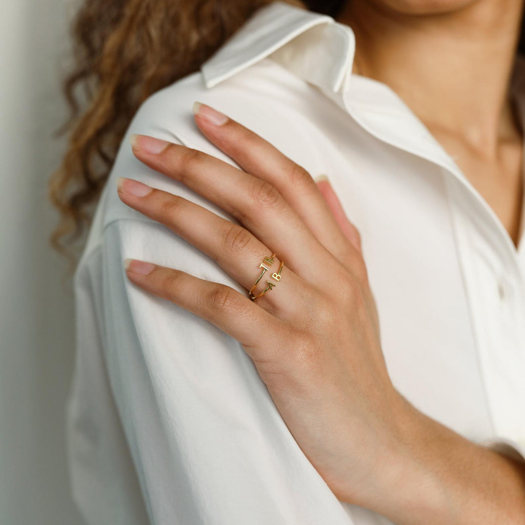 A woman in a white shirt displays her hand adorned with two gold rings, one of which is the stylish Modern Duo Initial Ring on her finger.
