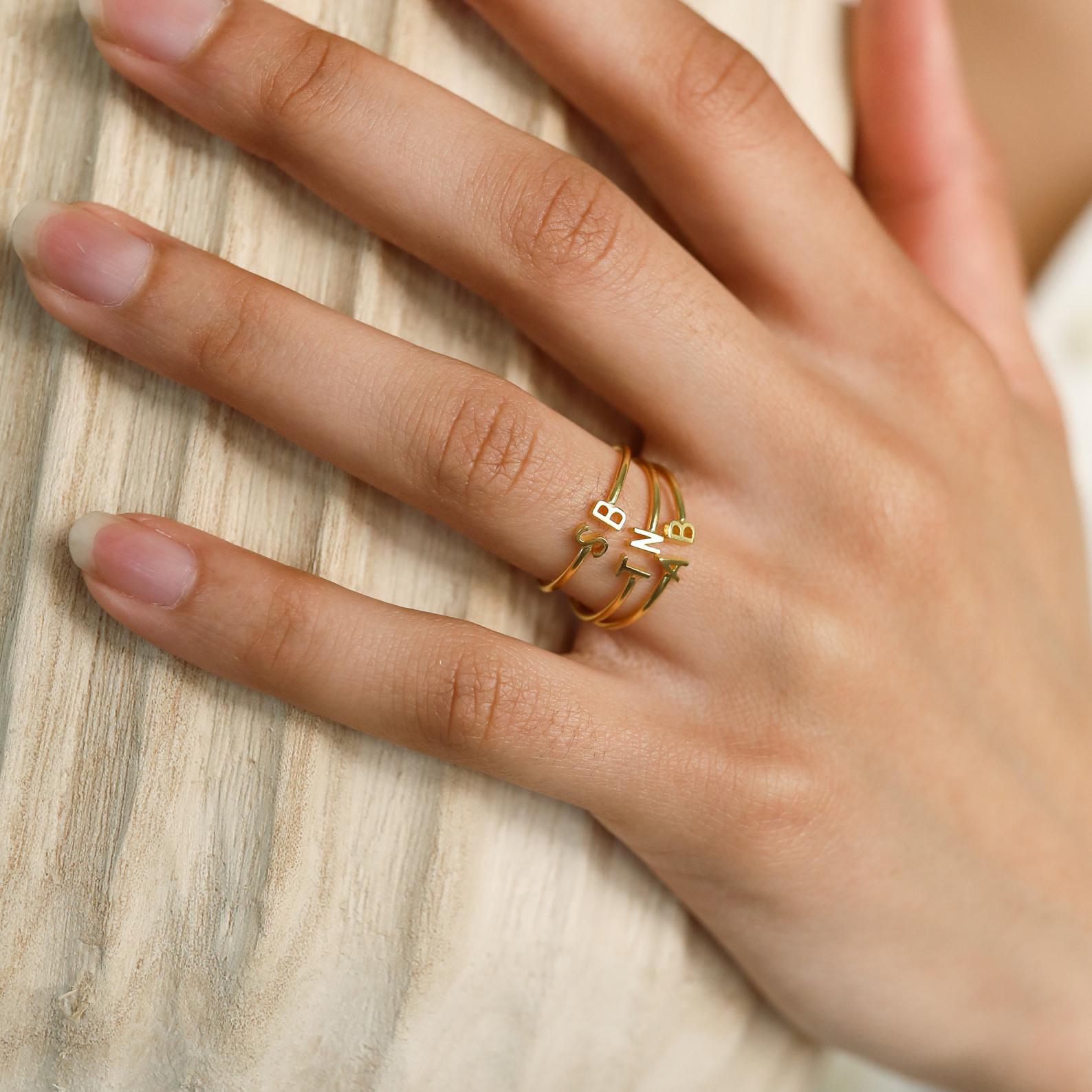 A hand with manicured nails showcases the Modern Duo Initial Ring—an elegant gold ring with minimalist, abstract accents—worn on the middle finger to highlight the sophistication of custom jewelry.