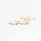 Two gold Modern Initial Birthstone Rings, each featuring an initial and a small gemstone, sit on a white surface—an ideal personalized gift for Christmas.