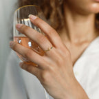 A woman holds a glass of rosé wine, displaying the Venice Initial Birthstone Ring adorned with two small stones on her finger.