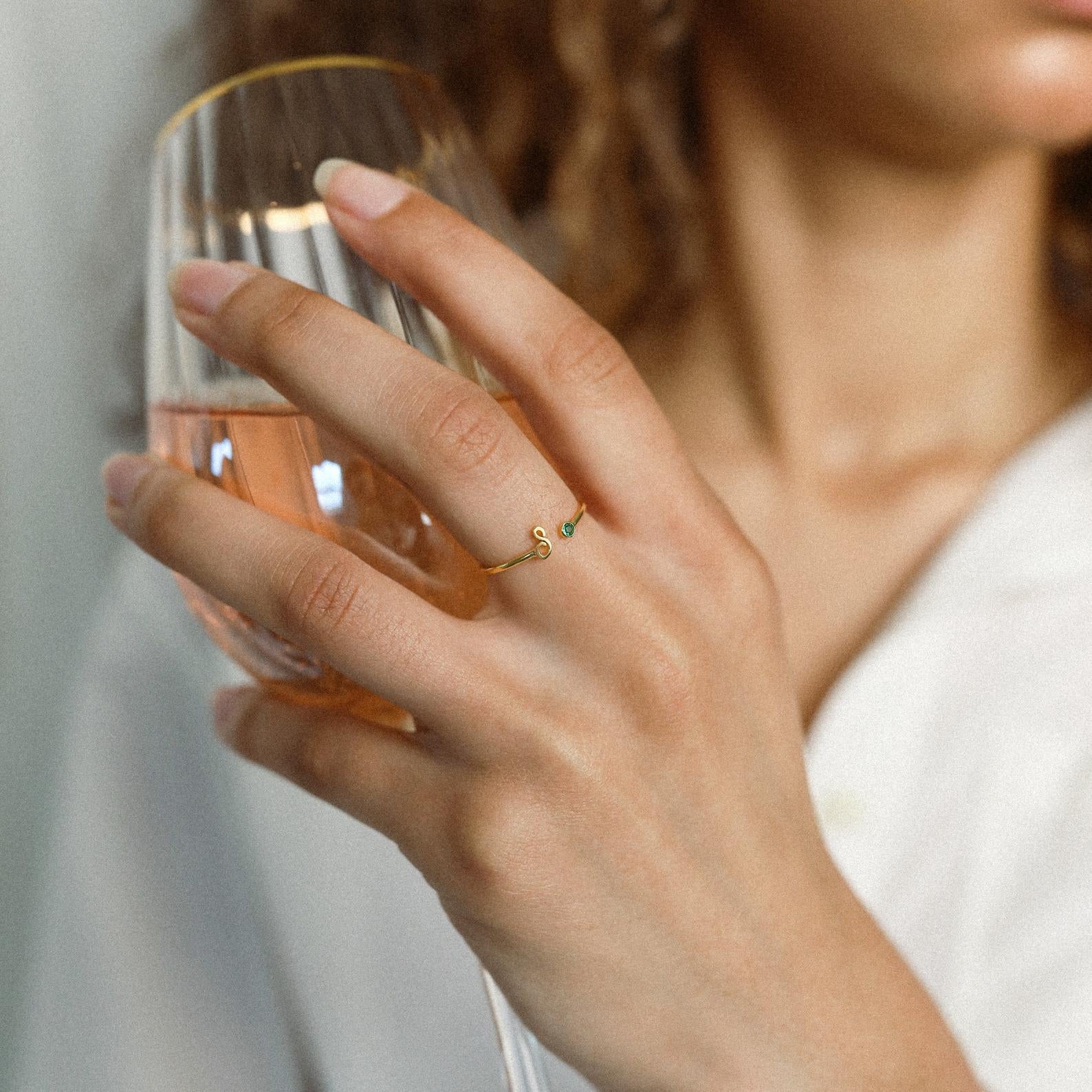 A woman holds a glass of rosé wine, displaying the Venice Initial Birthstone Ring adorned with two small stones on her finger.