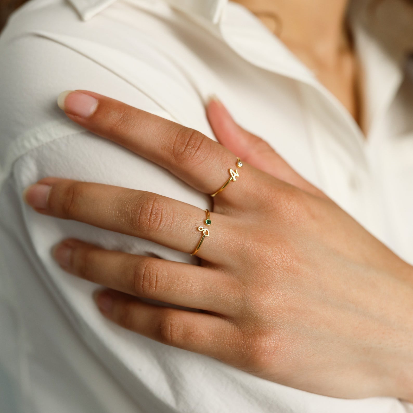 A hand with two Venice Initial Birthstone Rings, each personalized with small initials, resting on a white sleeve.