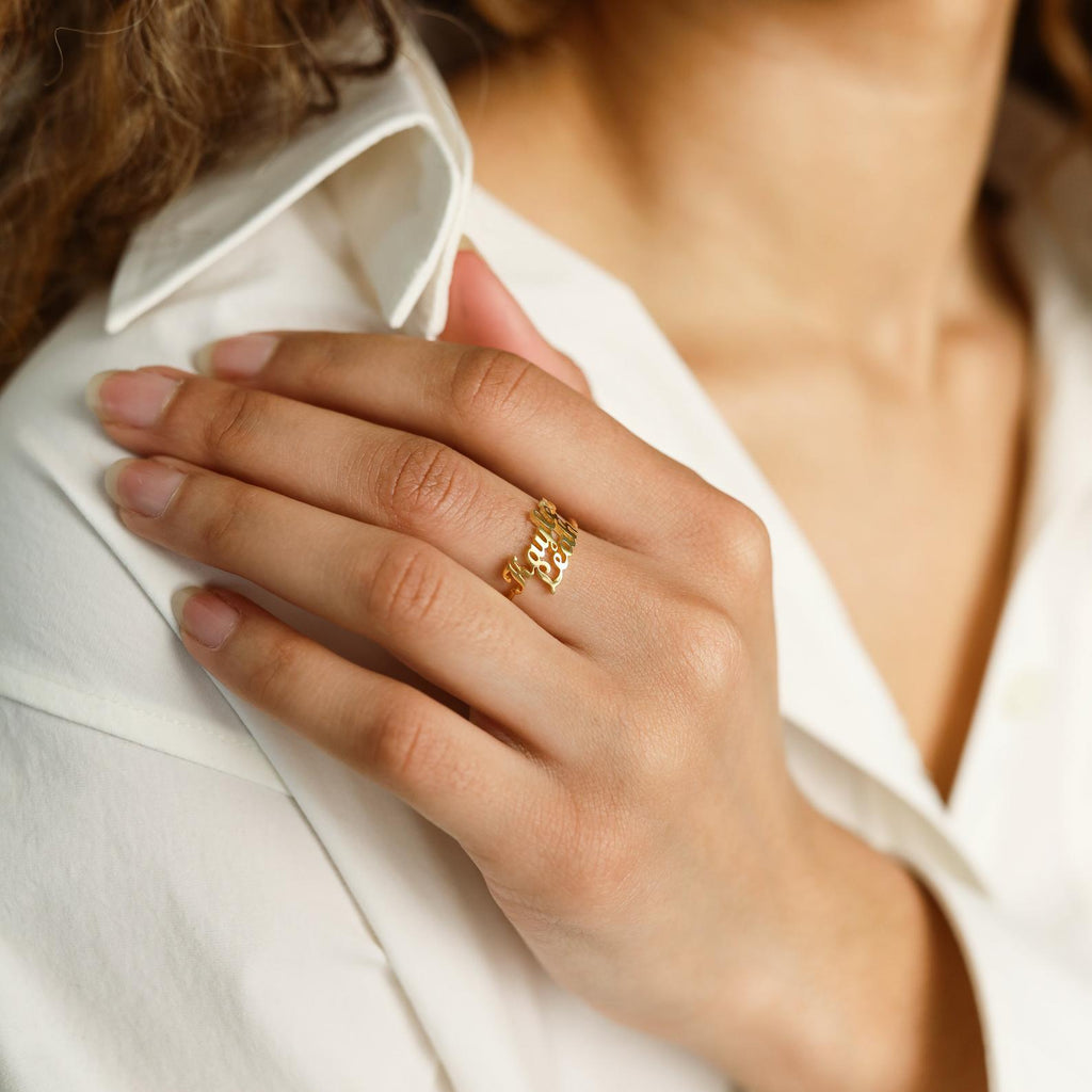 A hand wearing the London Duo Name Ring rests on a white shirt, highlighting neatly manicured nails and curly brown hair.