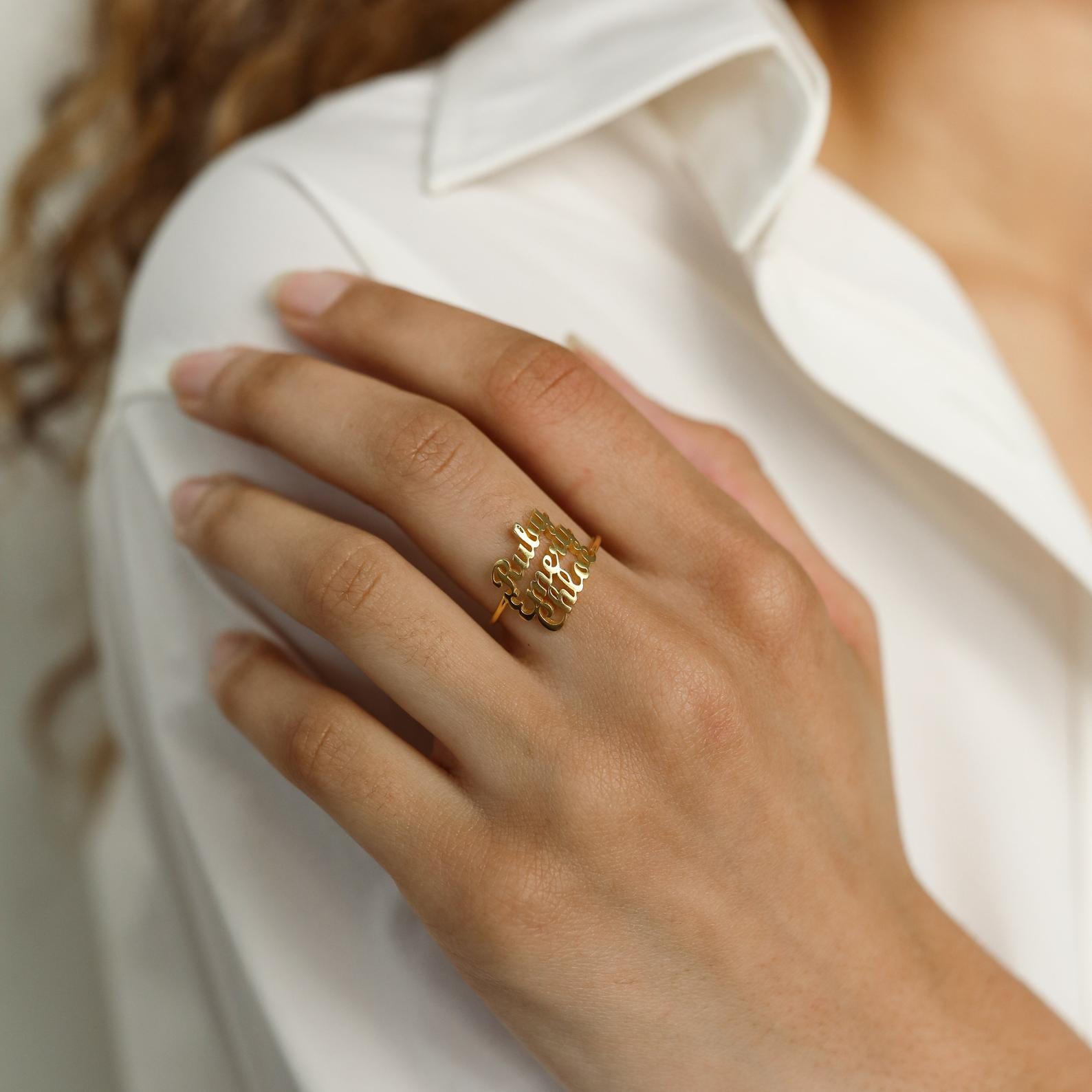 A hand adorned with the London Triple Name Ring rests on a white shirt, highlighting neatly manicured nails and stylish personalized jewelry.
