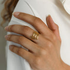 A hand with neatly manicured nails wears the London Triple Name Ring in gold, engraved with custom names, resting on a white shirt—ideal for fans of personalized jewelry.