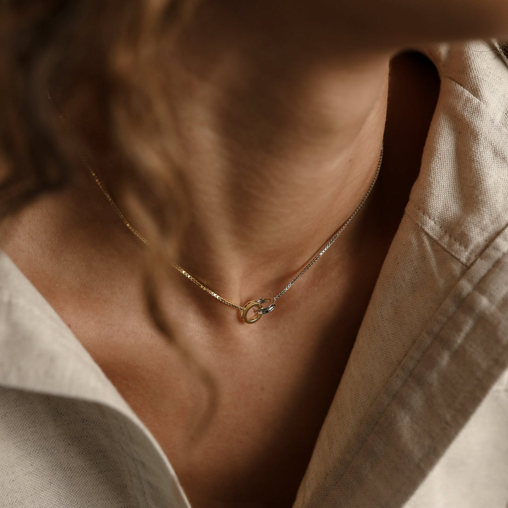 Close-up of a person wearing the Interlocking Circles Necklace in gold and silver with a beige collared shirt.