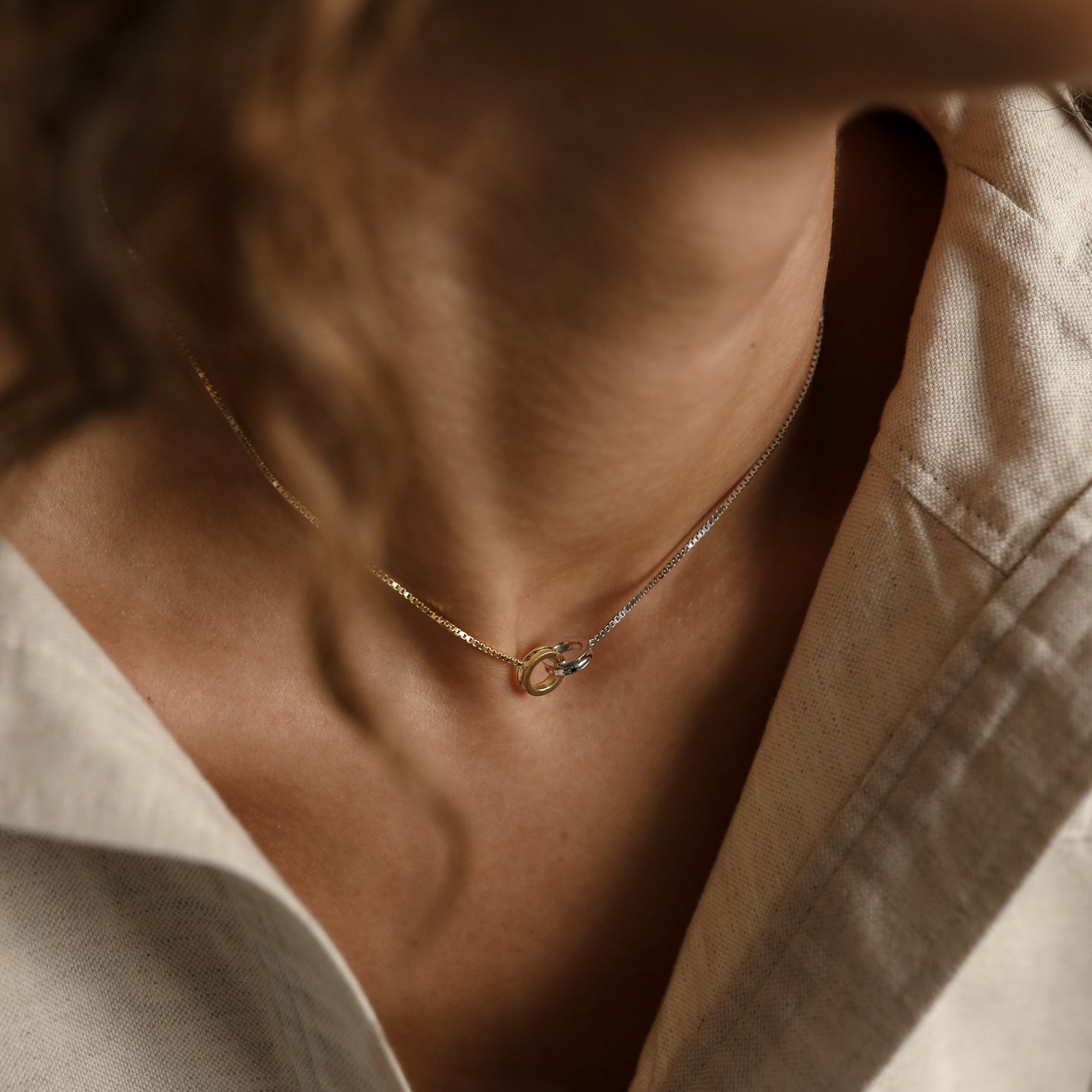 Close-up of a person wearing the Interlocking Circles Necklace in gold and silver with a beige collared shirt.