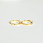 Two Alice Thin Engraved Rings rest on a white surface, each customized with names—a perfect personalized gift.