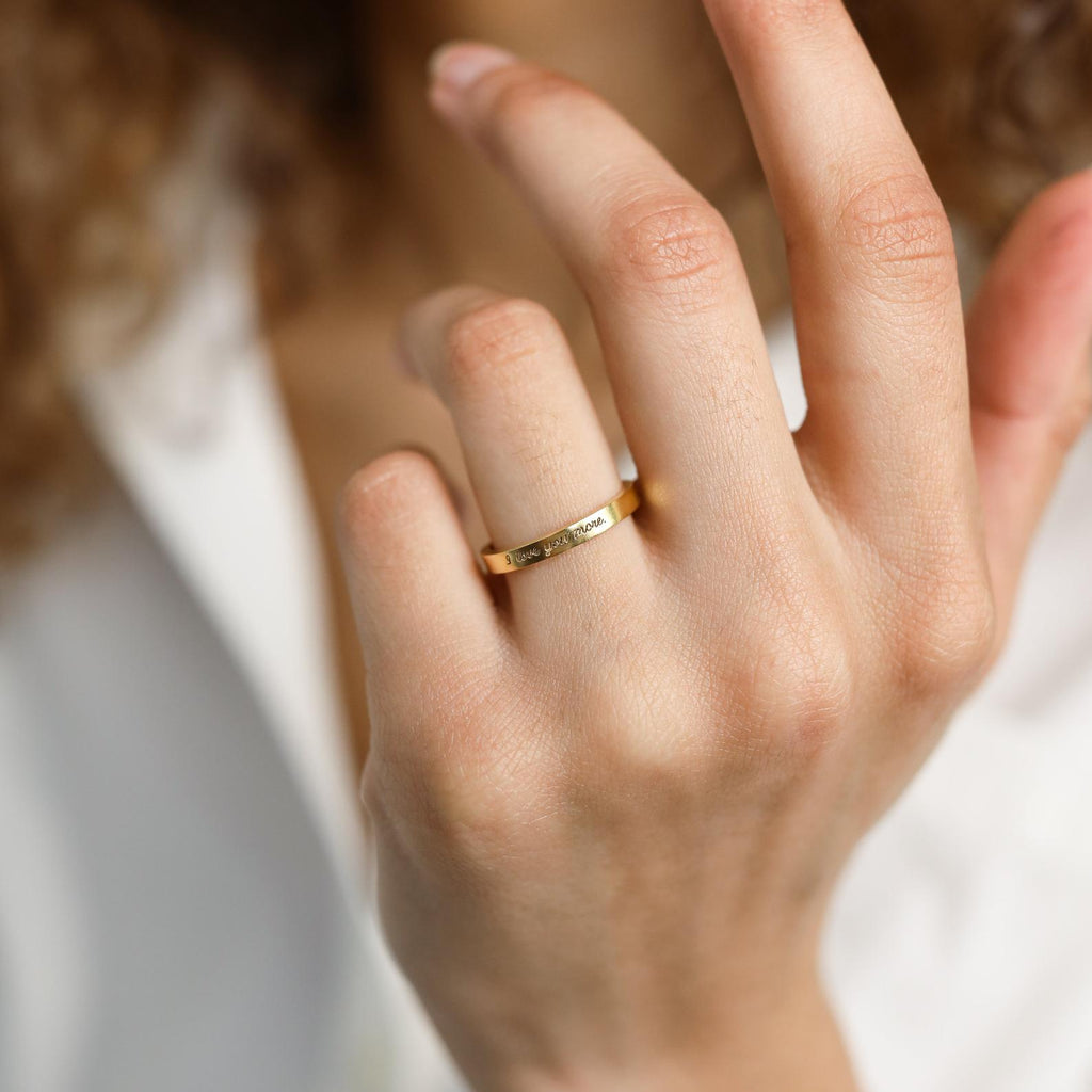 A hand wearing the Ann Thin Message Ring in Rose Gold, with a blurred white shirt in the background—an ideal, thoughtful holiday gift.