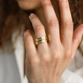A hand wearing the Ann Engraved Name Ring—a gold double-band ring personalized with the names Namala and Delilah.